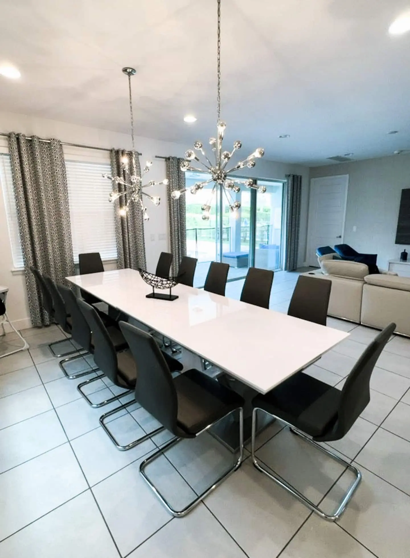 Long white dining table for twelve under sputnik chandeliers