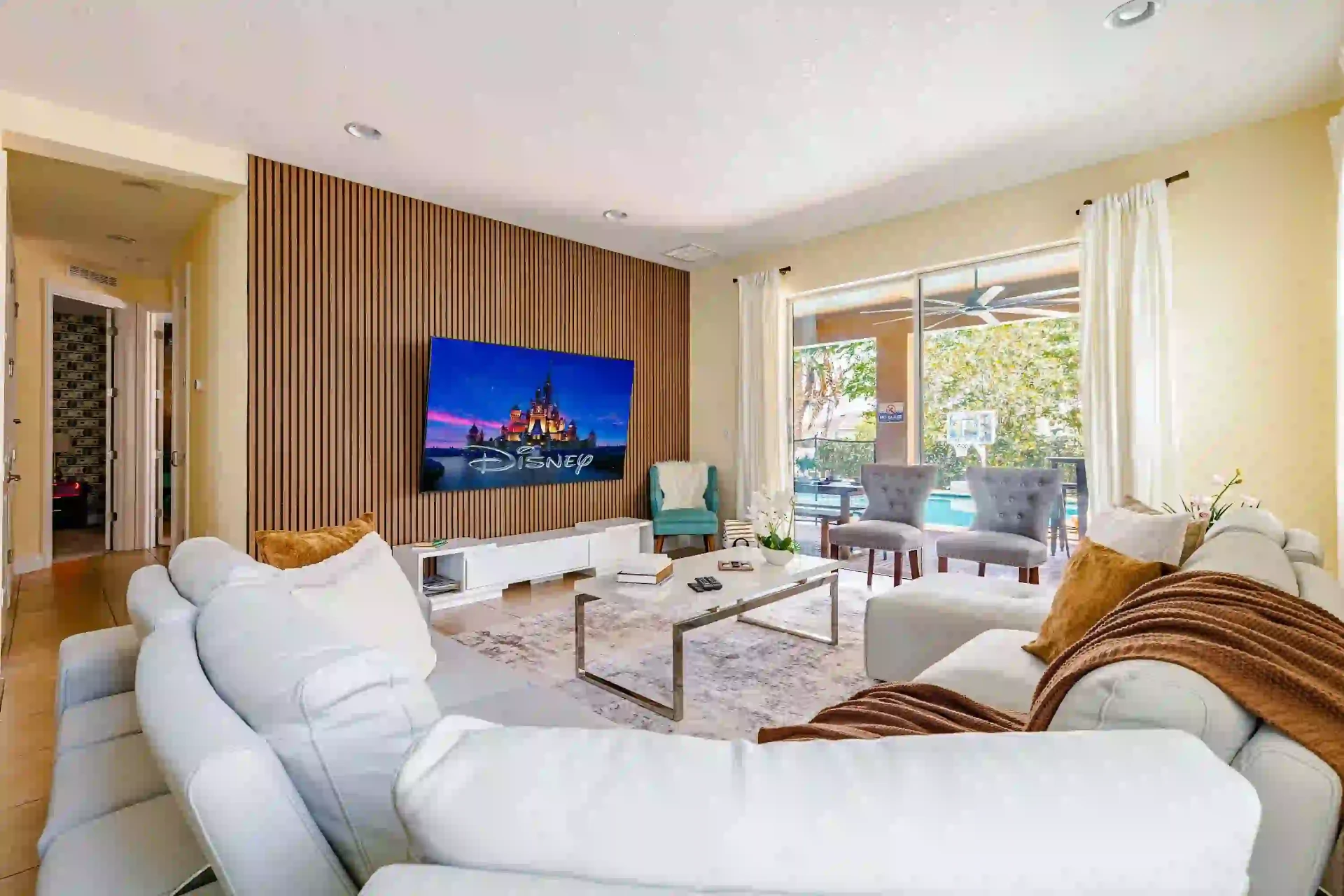 Living room with white sectional, Disney feature wall and pool view